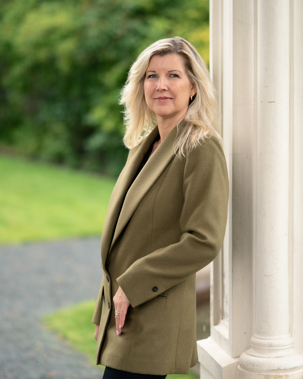 Woman in a green coat standing outdoors with a blurred background